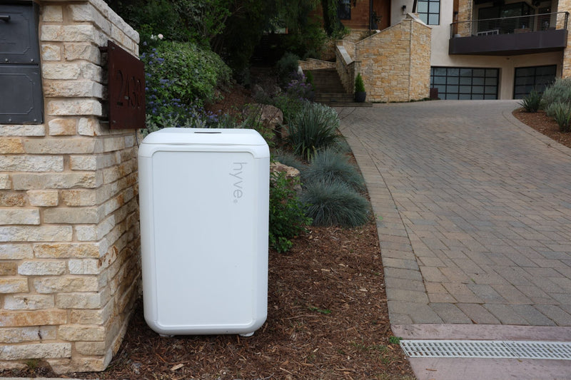 A white hyve smart package locker standing beside a stone mailbox pillar at the end of a home's driveway